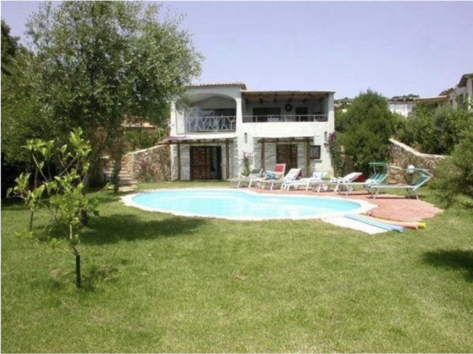 Immagine di una villa con piscina, circondata da un giardino verde e alberi, con lettini a bordo piscina.
